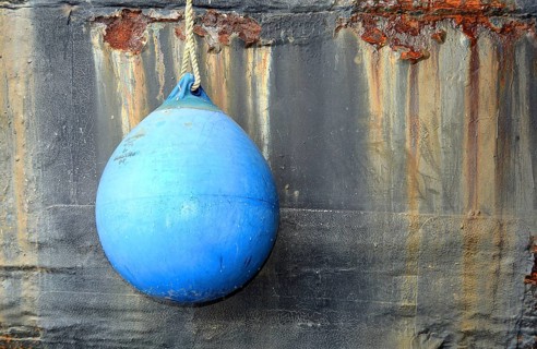 Blue fender in front of rusty ship's wall