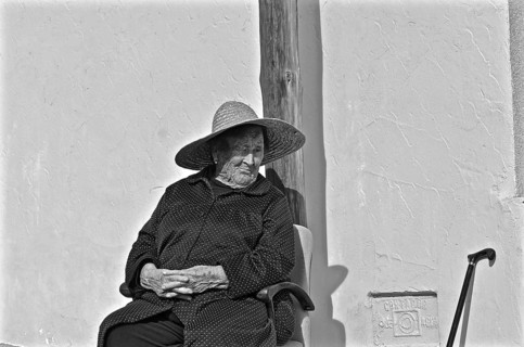 Old woman with folded hands sitting on chair with sun hat