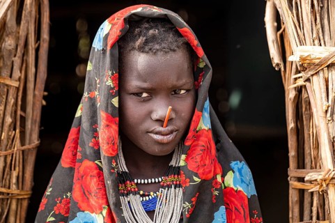 Traditional dressed child of the Jiye tribe sitting in her hut