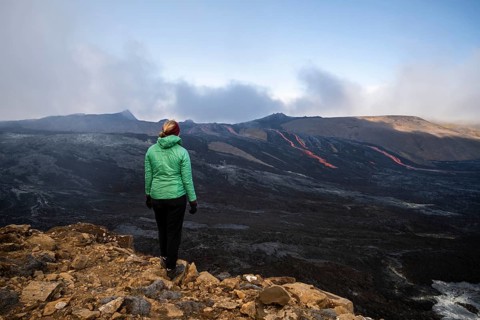 Tourist looking at erupting volcano with lava fountains and lava field