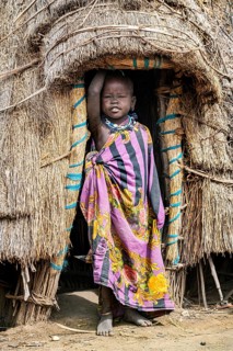 Traditional dressed child of the Jiye tribe standing in her hut