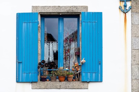 Closed window with blue wooden shutters with flowers in front and maritime anchor on the facade in Ville Close