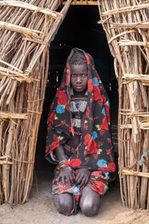 Traditional dressed child of the Jiye tribe sitting in her hut