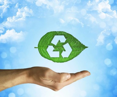 Opened hand holding a green leaf with recycling symbol on a blue sky background