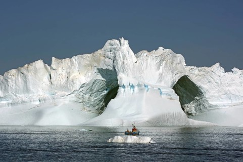 Small fishing boat in front of huge iceberg with two large caves