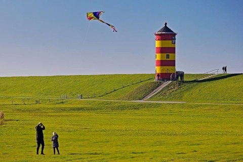 Girl flying a kite in front of the Pilsum lighthouse