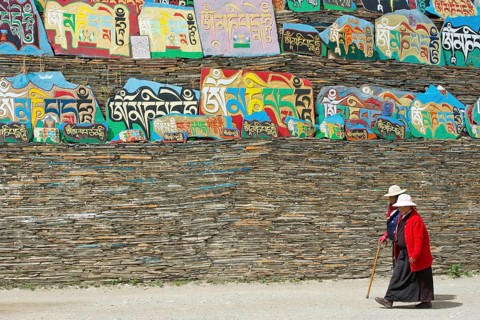 Two Tibetan women walking around a huge piled stack of mani stones with Tibetan writing at a Tibetan monastery in the grasslands of Tagong