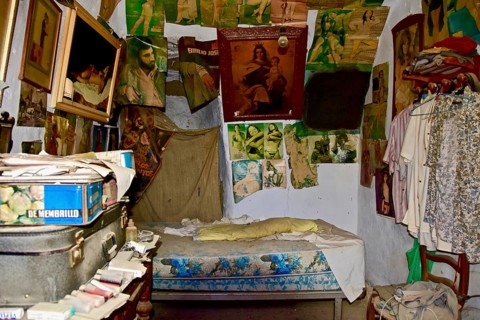 Bedroom with images of saints and photos of woman above bed in a cave dwelling