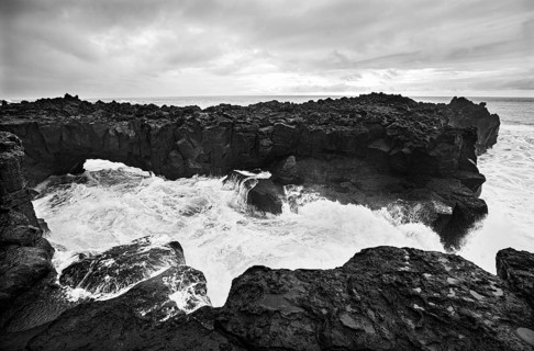 Lava arch on the volcanic coast at high tide with high waves