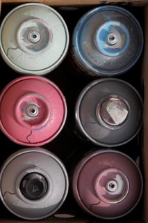 Six colourful spray cans in cardboard box
