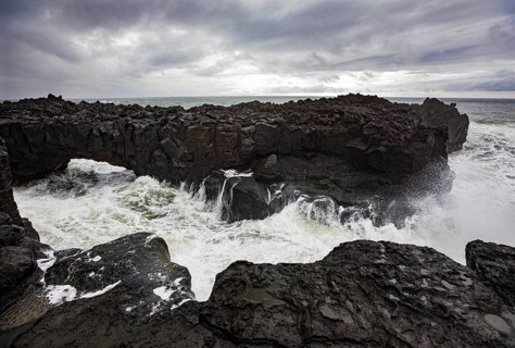 Lava arch on the volcanic coast at high tide with high waves