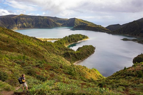 Hiker at the crater rim with view to the crater lake Lagoa do Fogo