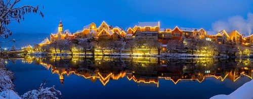 Christmas illuminated house facade of Frohnleiten reflected in the river Mur