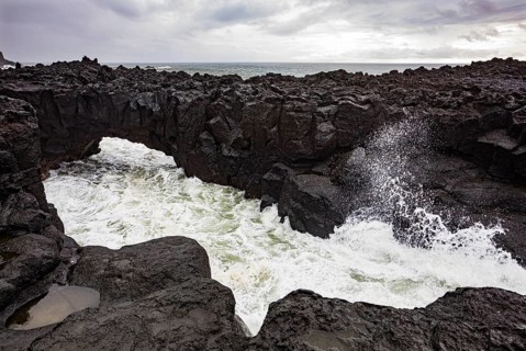 Lava arch on the volcanic coast at high tide with high waves