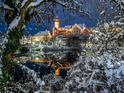 Christmas illuminated house facade of Frohnleiten reflected in the river Mur