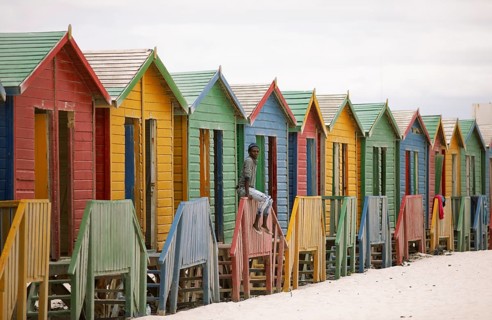 Man sitting on fence in front of colourful beach huts