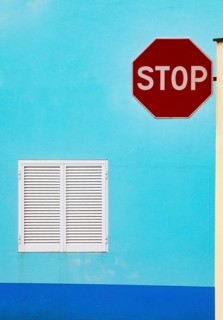 Light blue house facade with closed white shutters and stop sign