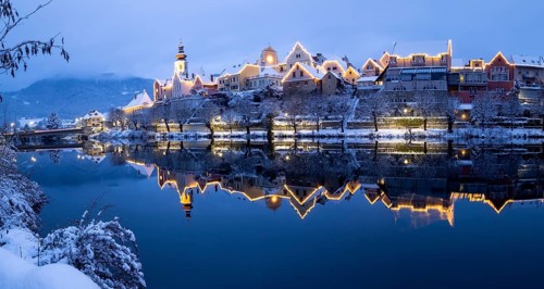 Christmas illuminated house facade of Frohnleiten reflected in the river Mur