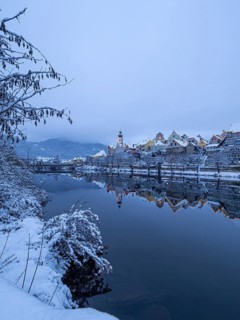Christmas illuminated house facade of Frohnleiten reflected in the river Mur