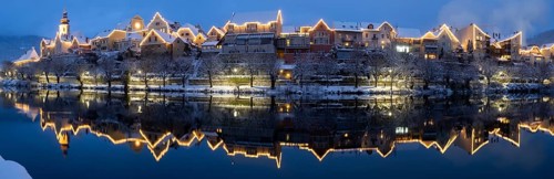 Christmas illuminated house facade of Frohnleiten reflected in the river Mur