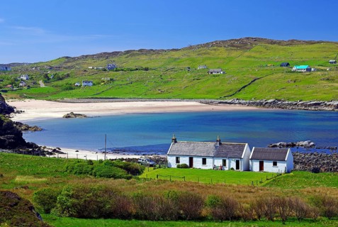 Small cottage in front of long sandy beach in green landscape
