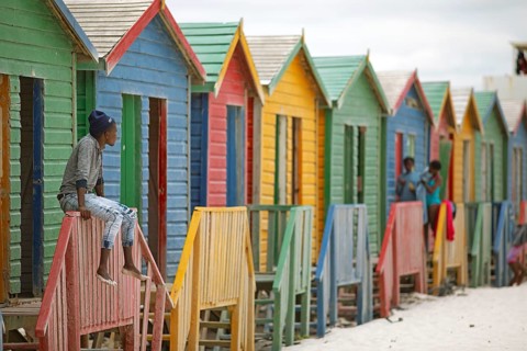 Man sitting on fence in front of colourful beach huts