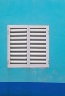Light blue house facade with closed white shutters