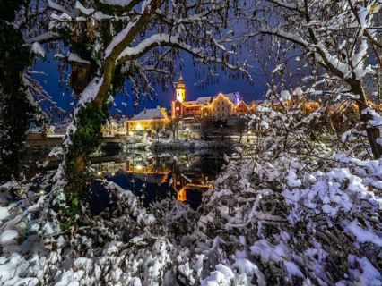 Christmas illuminated house facade of Frohnleiten reflected in the river Mur