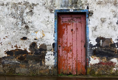Weathered house facade with old closed red front door in Porto Formoso