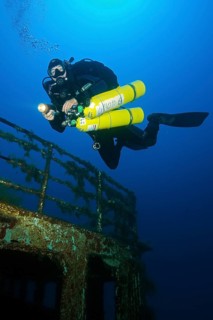 Diver swims over shipwreck has special equipment carries stage tanks for mixed gas diving