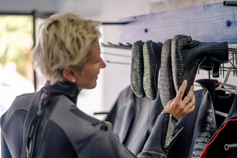 Blond woman in wetsuit choosing boots for water adventure