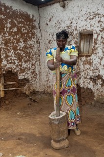 Woman grinding cassava with a post and wooden pot to create Cassava flour to be used in baking. Rwanda