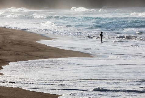 A woman standing on the sandy beach of Praia de Santa Barbara in stormy sea with high waves