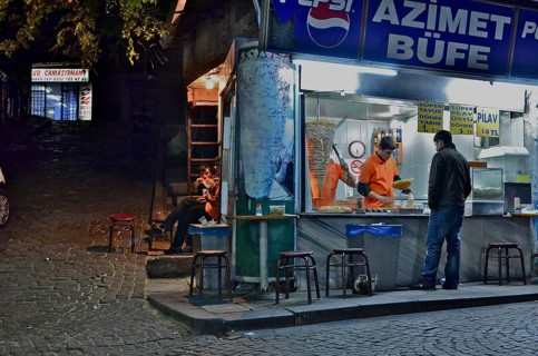 Kebab shop illuminated at night with vendor and customers