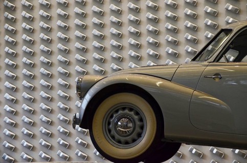 Grey vintage car with whitewall tyres in front of Audi design wall
