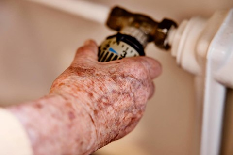 Hand of a senior citizen with age spots on the thermostat of a heater