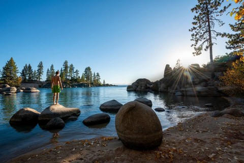 Young man in swimming trunks standing on a round stone in the water