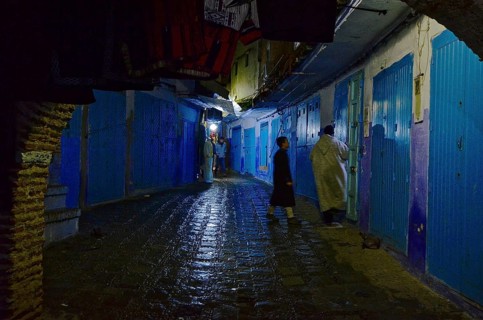 Shopkeepers close door in sparsely lit alley with closed shops at night