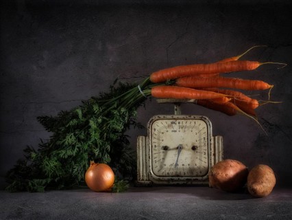 Still life with carrots on old kitchen scales next to onions and sweet potatoes