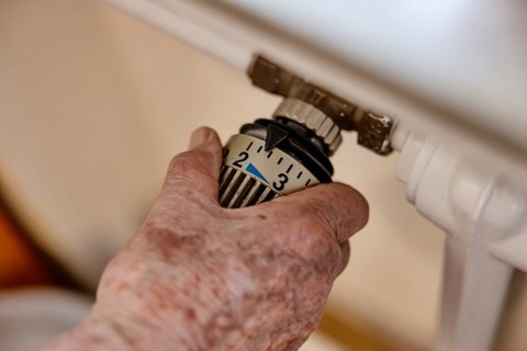 Hand of a senior citizen with age spots on the thermostat of a heater