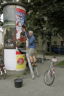 Man on ladder sticking poster on advertising pillar