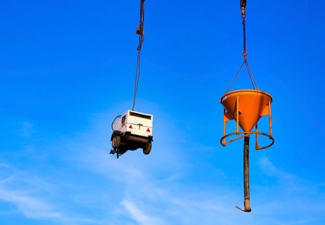 Construction machinery chained to a construction crane against a blue sky
