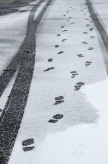 Traces of car tyres and footprints on thin snow cover of asphalt road