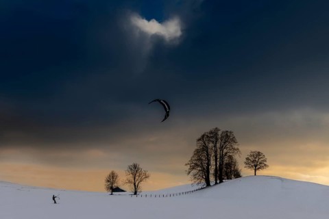 Kite surfers in winter landscape in front of dramatic sky