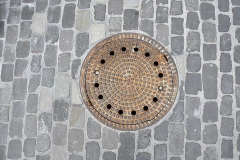 Round iron manhole cover in cobblestones