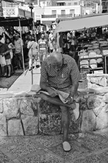 Old man reading newspaper on wall in front of market