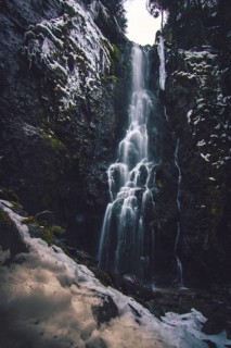 The Burgbach waterfall with snow in winter. Waterfall with stone steps in Schapbach