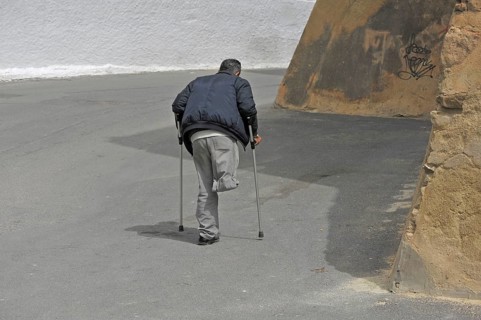 Disabled one-legged man on crutches walks in the street