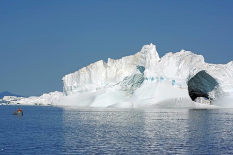 Small fishing boat in front of huge iceberg with two large caves