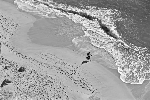 Man with guitar on lonely beach with footprints in sand